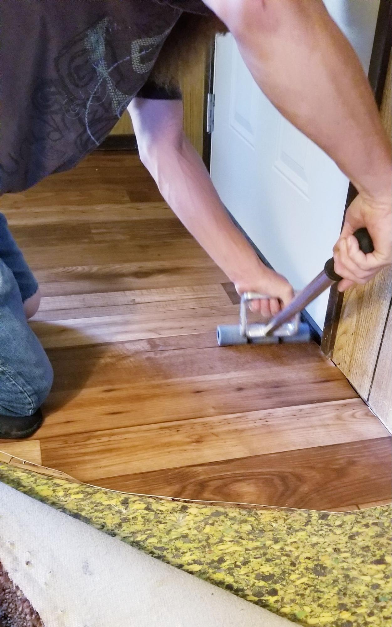 Hardwood flooring installation in progress as a worker removes old flooring with hand tools.