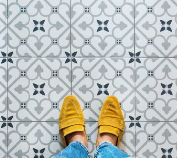 Top view of female feet in yellow shoes standing on a vibrant ceramic mosaic tile floor 