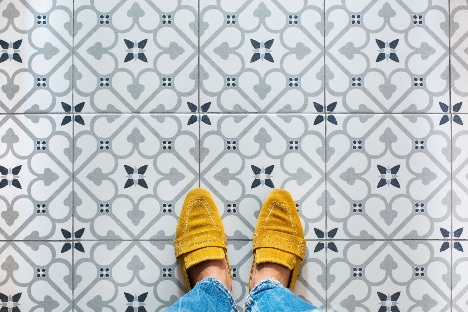 Top view of female feet in yellow shoes standing on a vibrant ceramic mosaic tile floor.