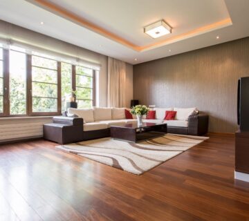 L shaped sofa and rug on rich, dark solid hardwood flooring in a modern living room with expansive glass windows 
