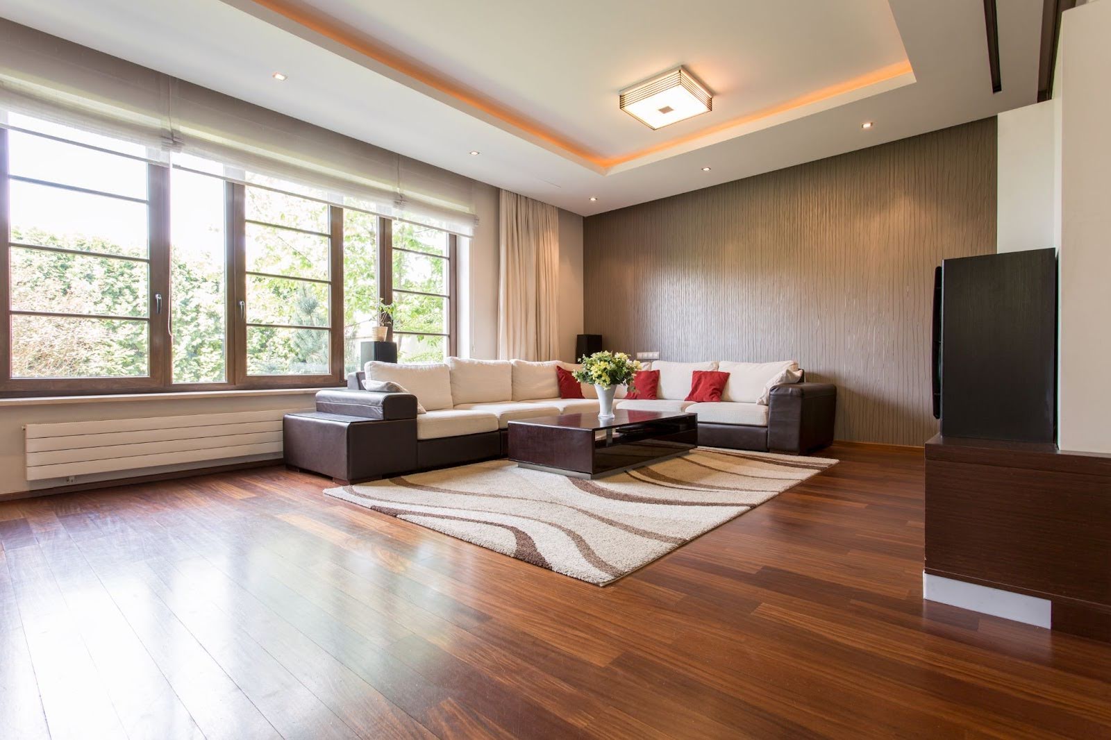 L-shaped sofa and rug on rich, dark solid hardwood flooring in a modern living room with expansive glass windows.